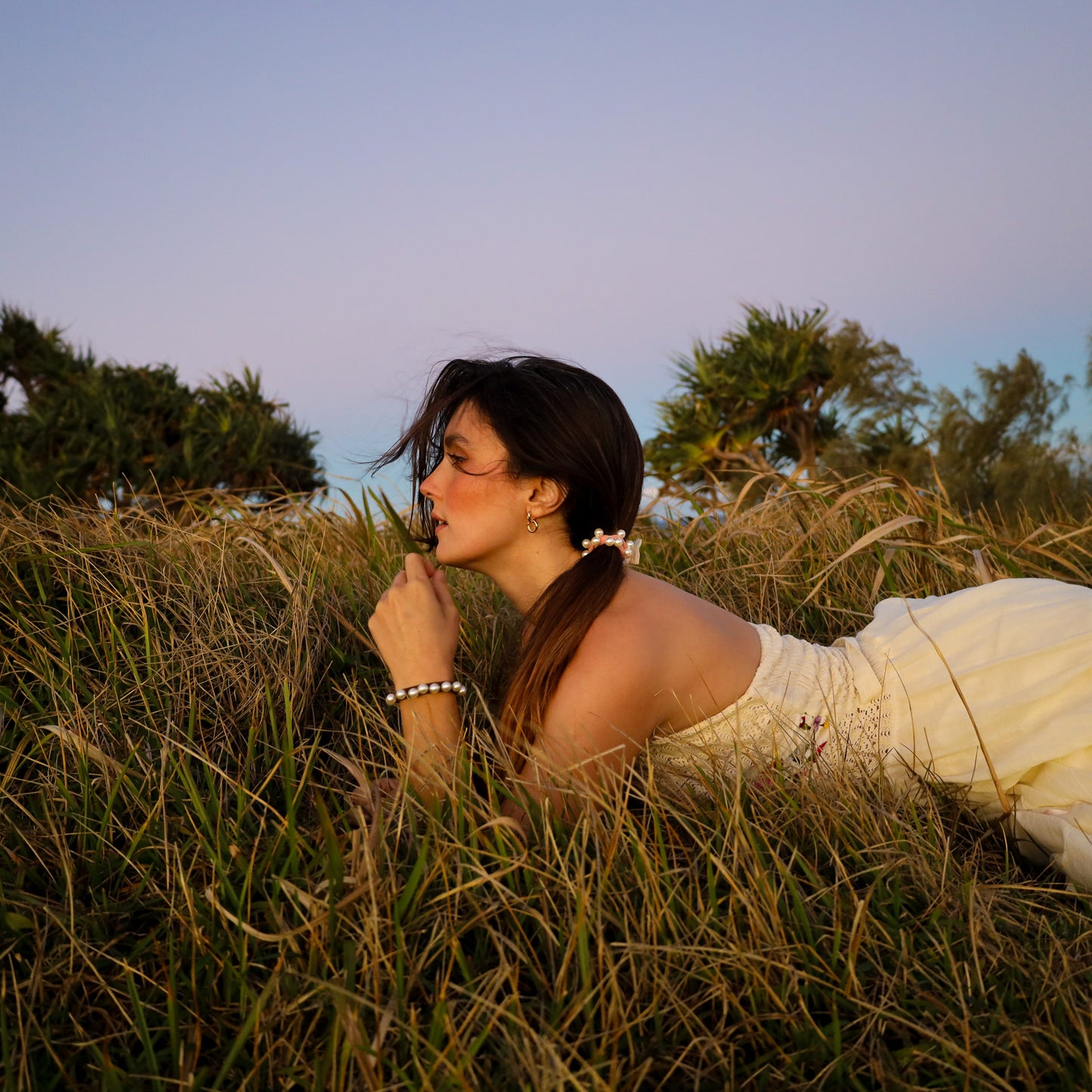 Woman in a white dress lying in tall grass with trees in the background