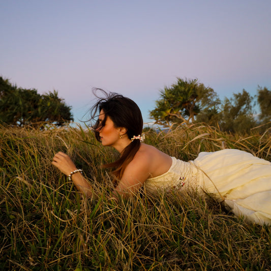Woman in a white dress lying in tall grass with trees in the background