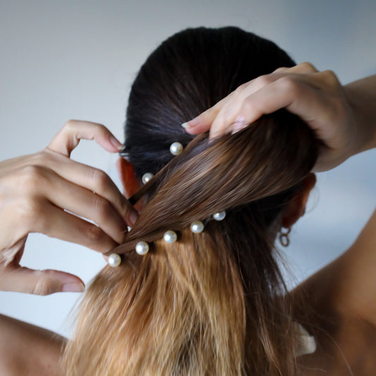 Person styling hair with pearl hair ties against a neutral background