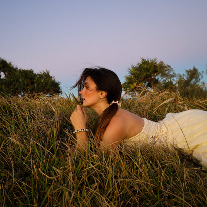 Woman in a white dress lying in tall grass with trees in the background