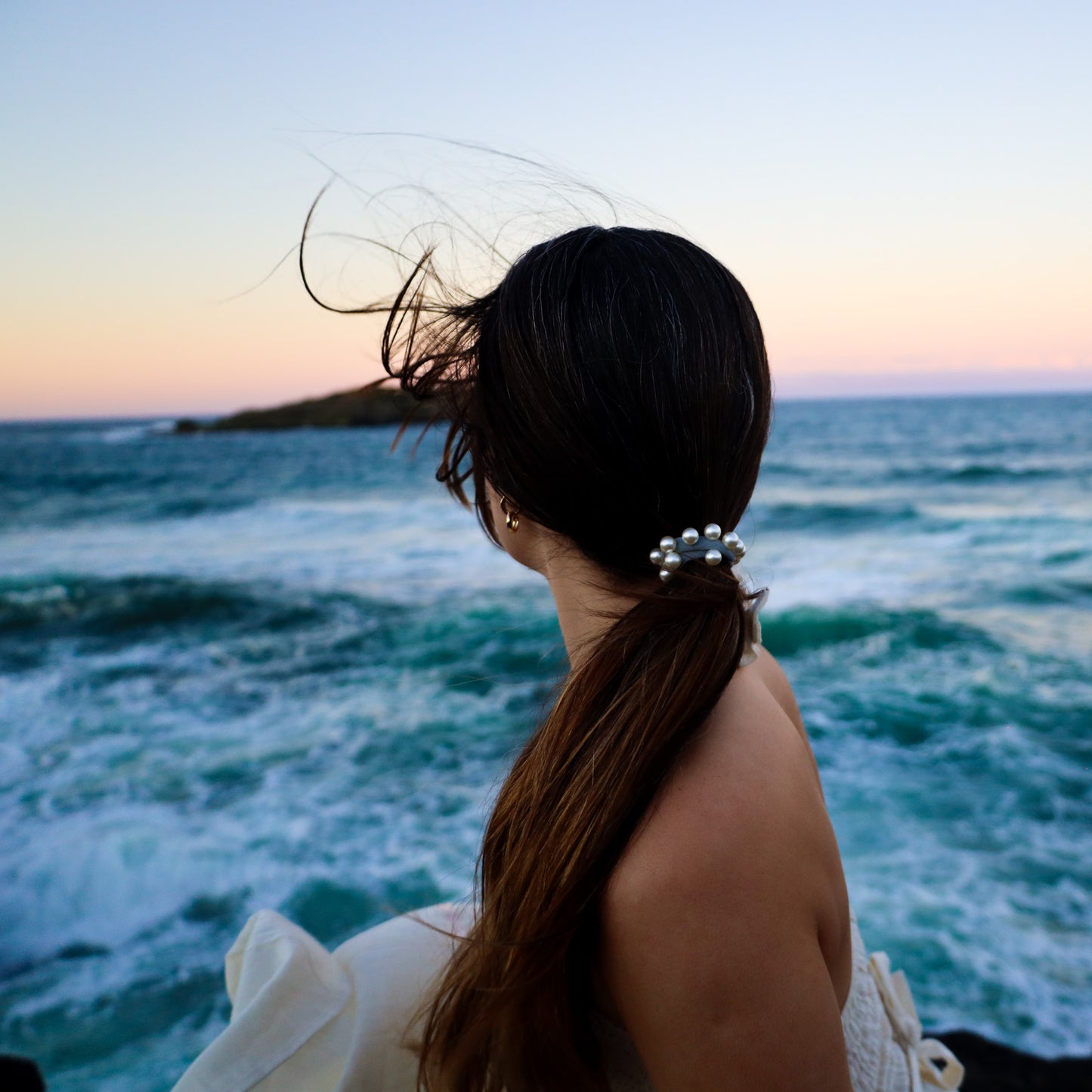 Woman with hair tied back, sitting by the ocean at sunset