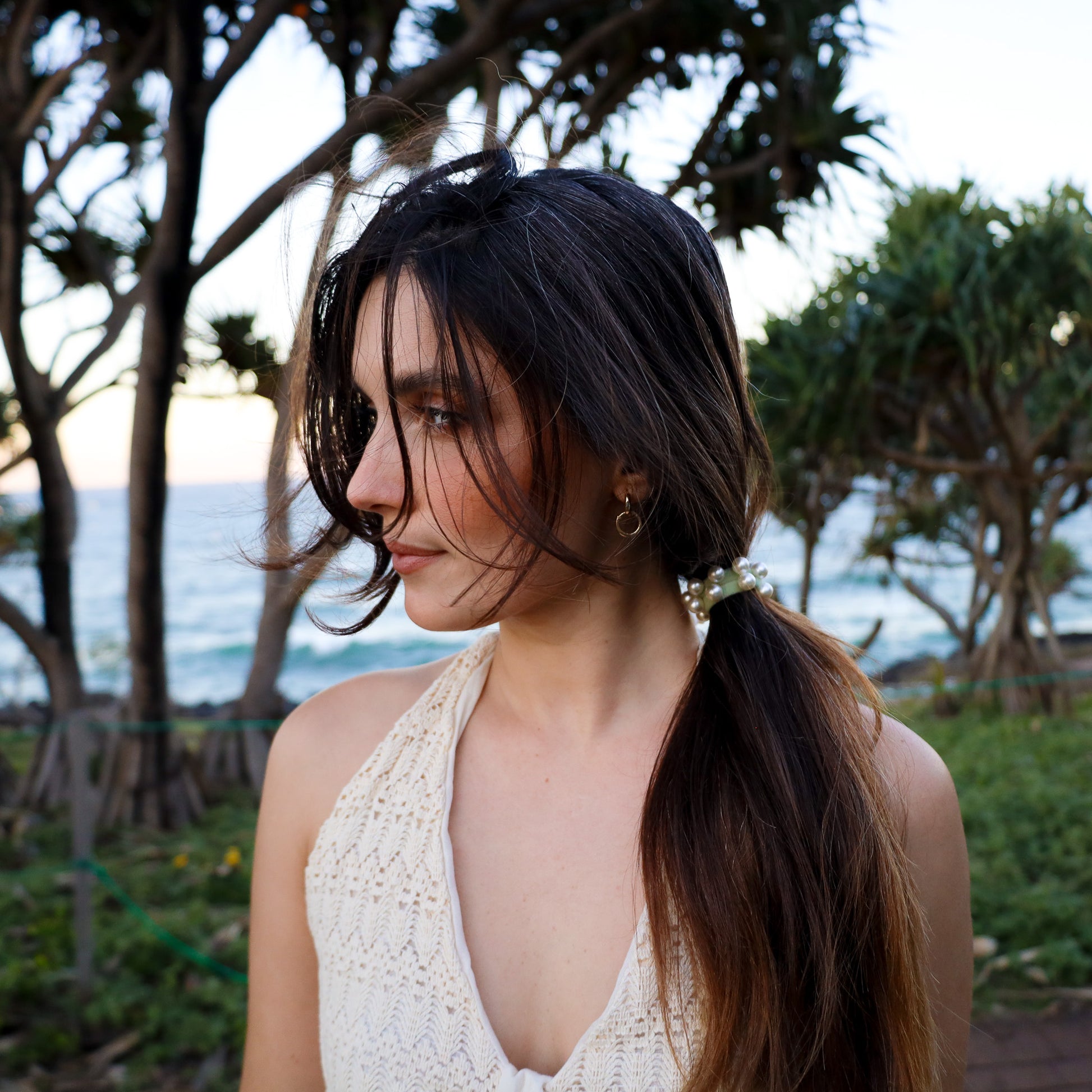 Woman with a ponytail standing outdoors with trees and ocean in the background