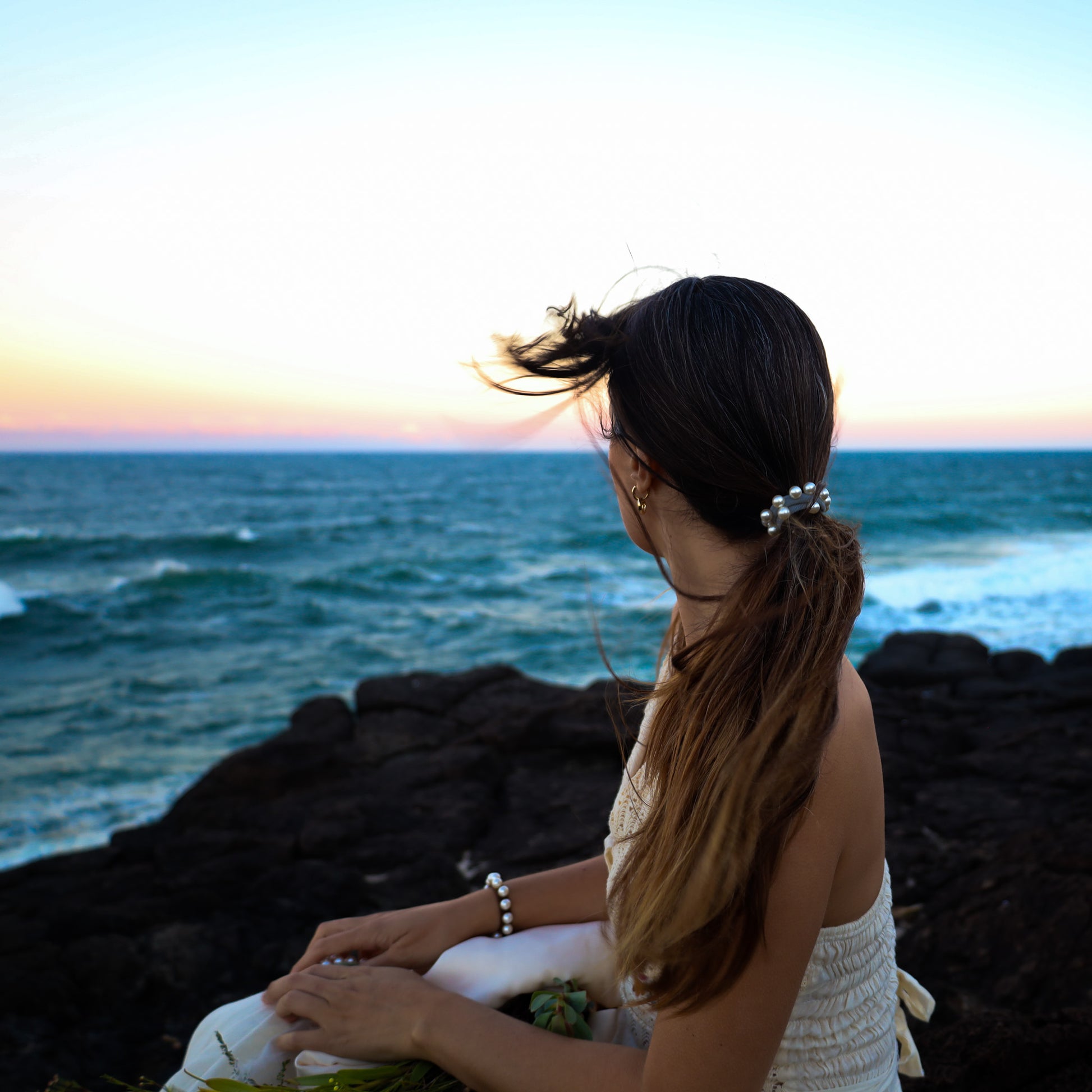 Woman sitting on rocks by the ocean at sunset