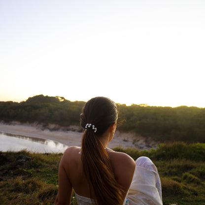 Woman sitting by the ocean at sunset, facing away from the camera.