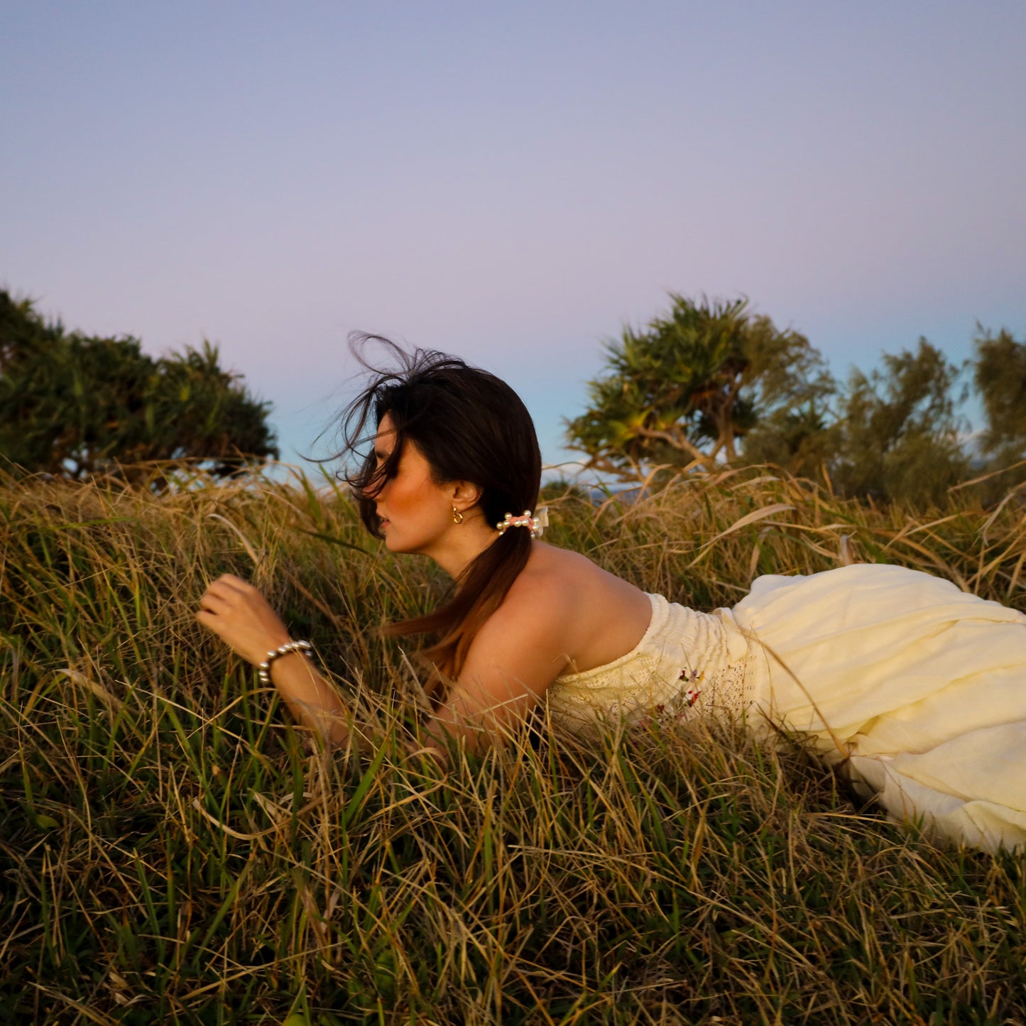 Woman in a white dress lying in tall grass with trees in the background