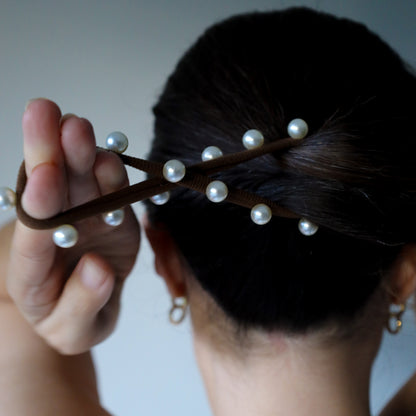 Person holding a hair tie with pearls against a neutral background